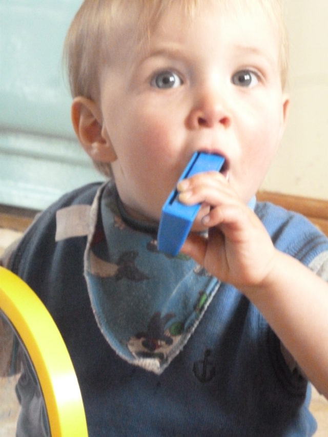 toddler cramming blue harmonica into his mouth
