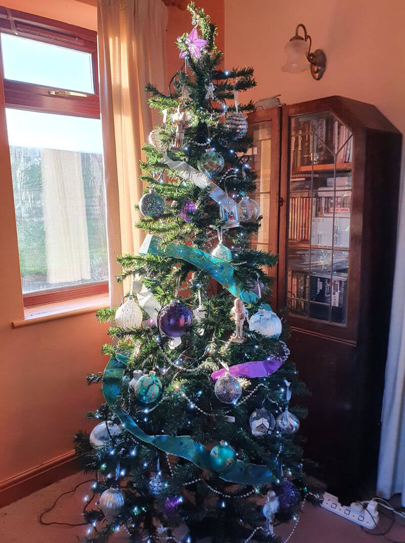 Christmas tree decorated in purple silver and teal green baubles and ribbon
