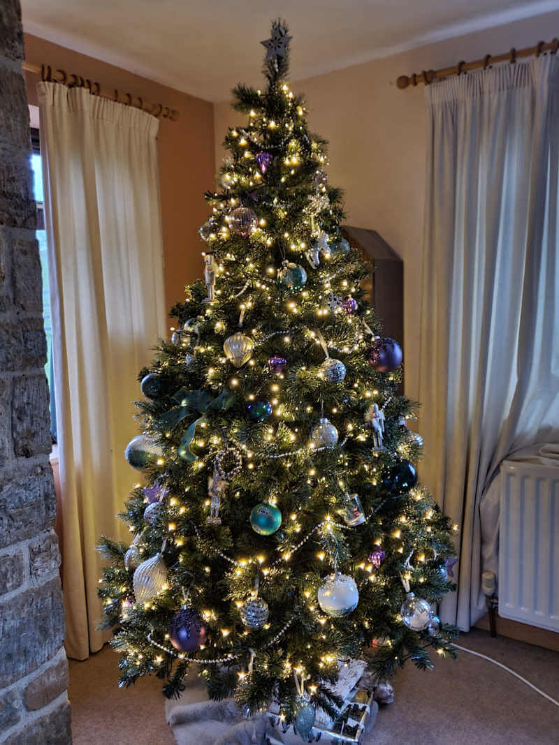 Lit up artificial 7ft christmas tree with baubles in living room corner