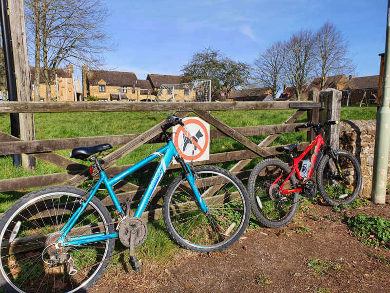 2 bikes leaning against wooden gate to a villate green playground