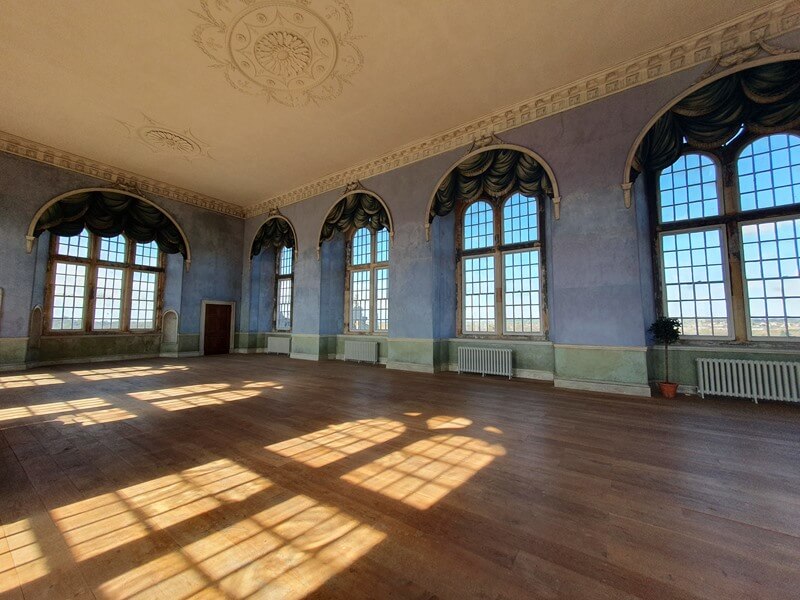 2 sides of prospect hall inside with arched windows and sun shining in to make window shadows on the wooden floor
