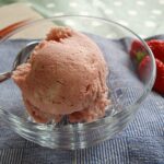 scoop of homemade strawberry ice cream in glass bowl with strawberries beside