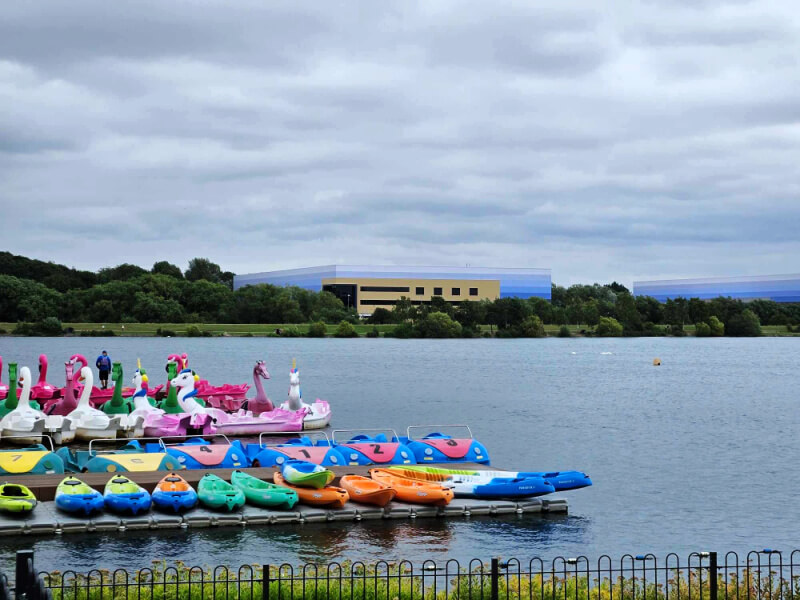 swan pedalos and boats on Willen Lake with factories behind on the skyline