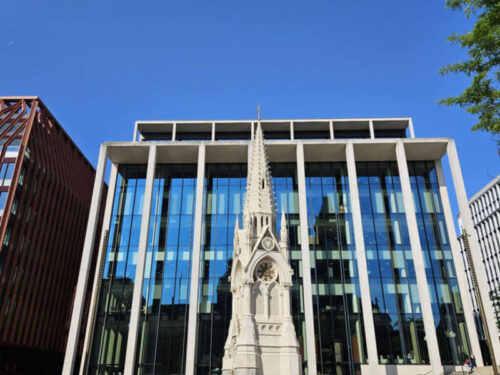 Spire statue in front of modern glass building